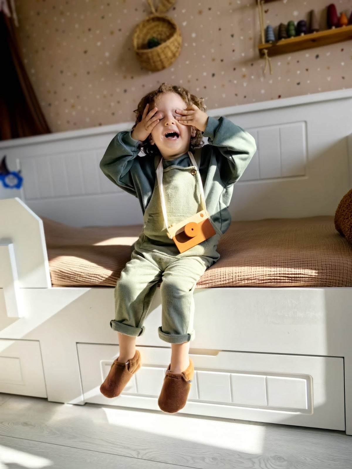 Child seated on a window seat with legs dangling in brown fleece moccasins.