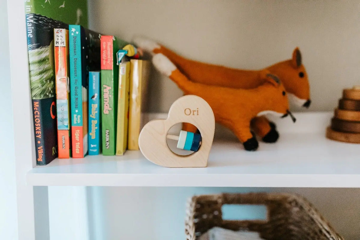 Heart-shaped wooden rattle with example engraving on a shelf beside books