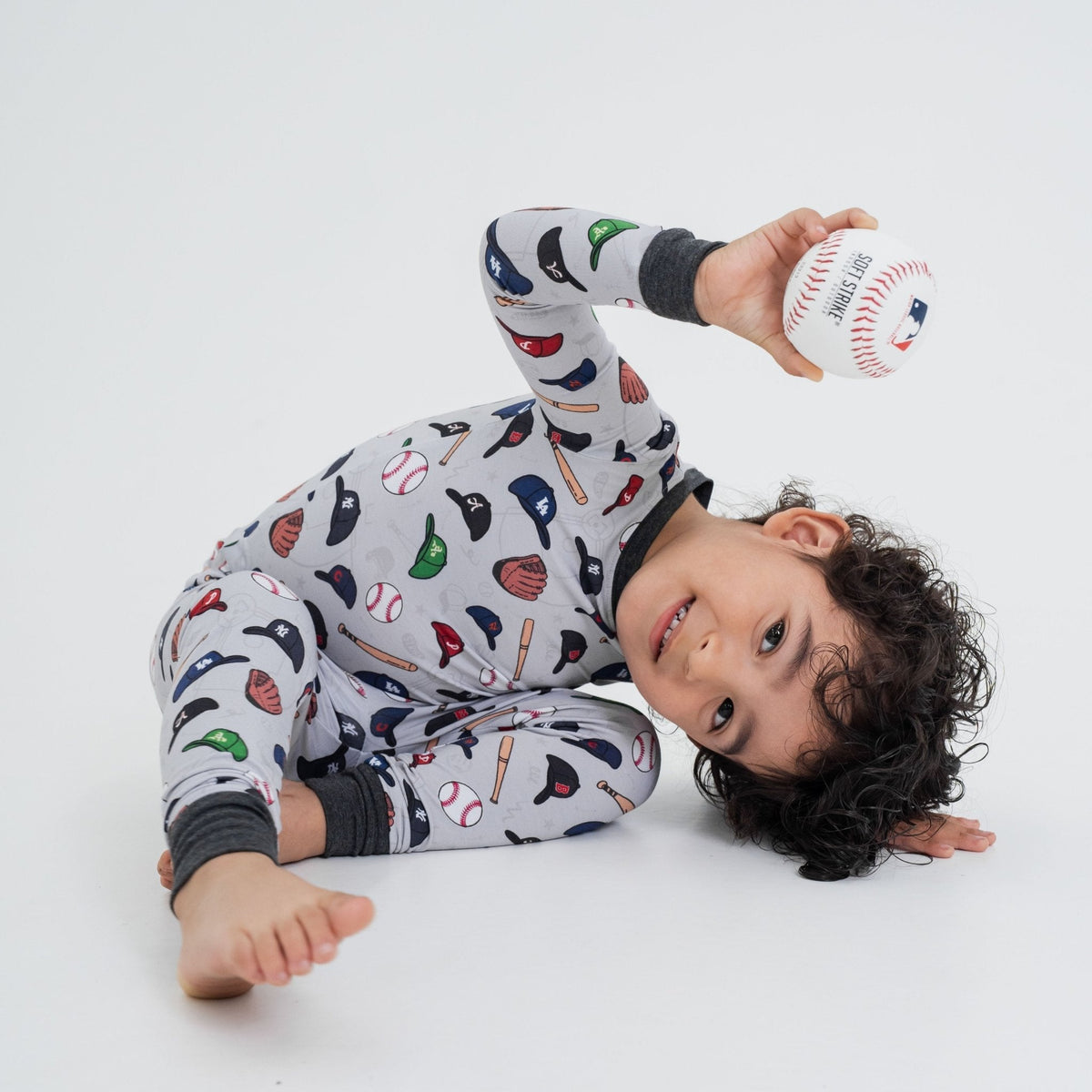 Child lying on the floor with a baseball while wearing Bam & Stitch Major League Buddies Long Sleeve Pajamas.