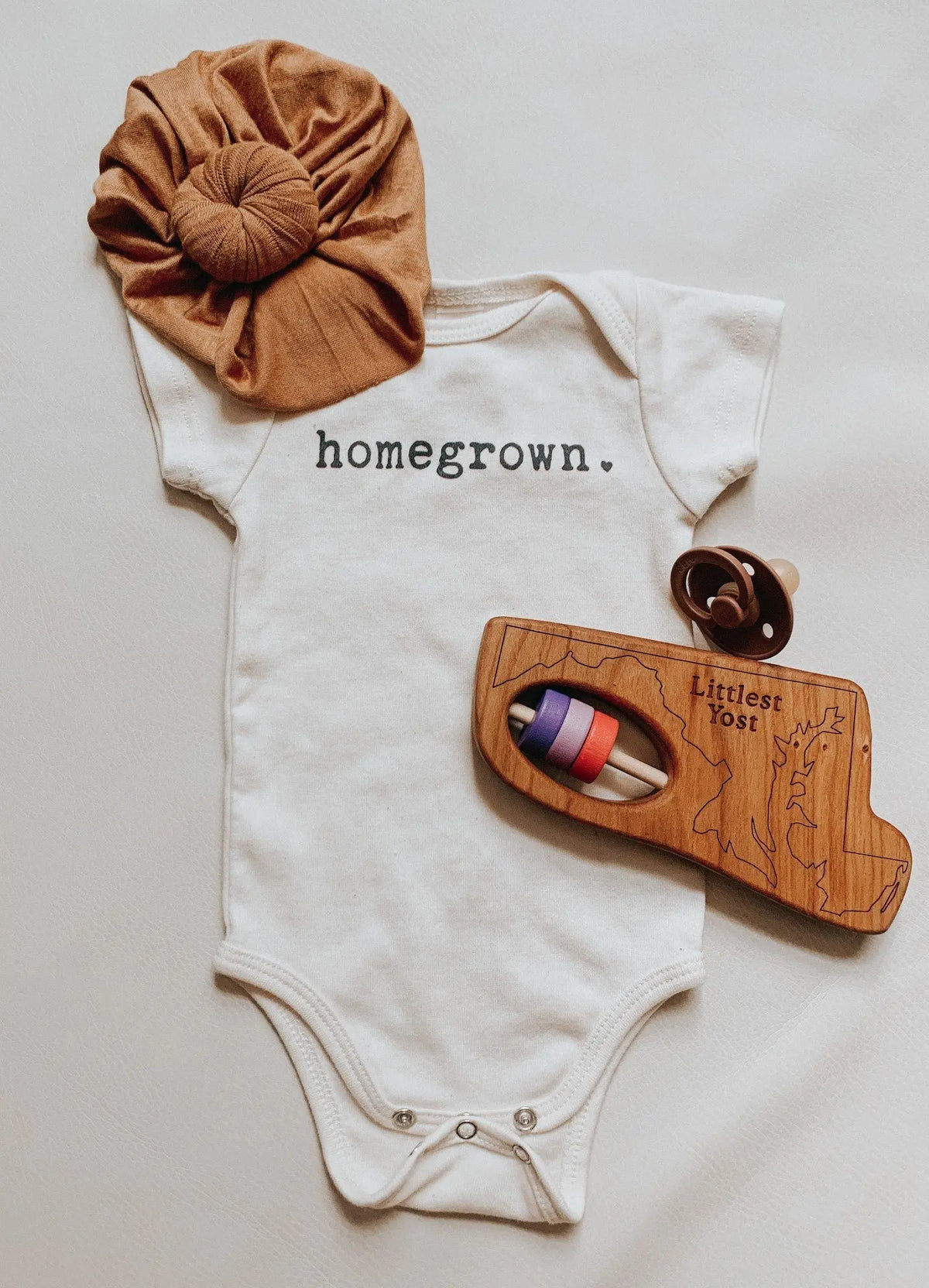 Maryland-shaped wooden rattle in a gift-style arrangement with baby clothing