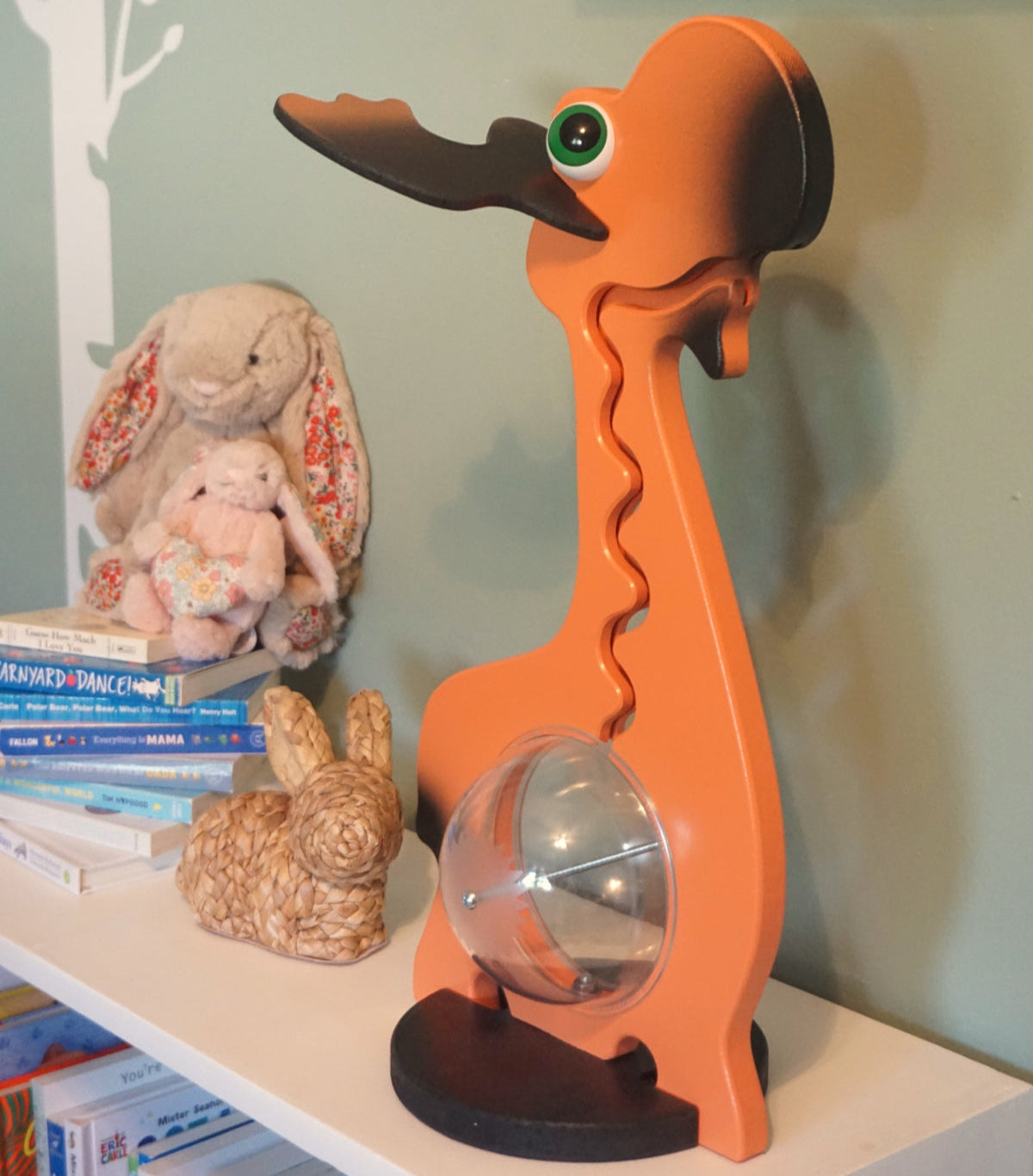 Moose coin bank displayed on a shelf beside books and a plush rabbit