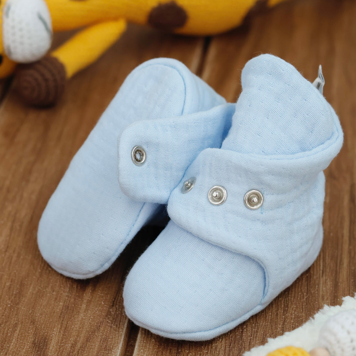 Close-up of light blue textured muslin baby booties with snap straps, showing one sole and an open snap strap.