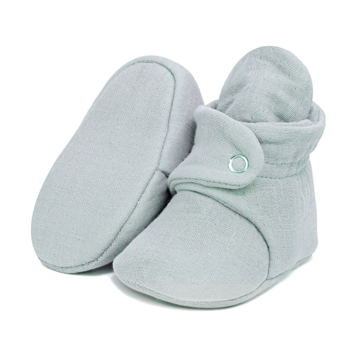 Light gray textured muslin baby booties with snap straps, with one sole facing the camera on a white background.