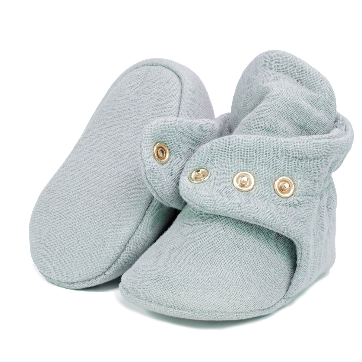 Light gray textured muslin baby booties with snap straps, showing one sole and an open snap strap on white.