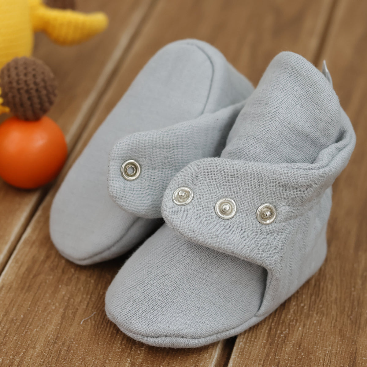 Close-up of light gray textured muslin baby booties with snap straps, showing one sole and an open snap strap.