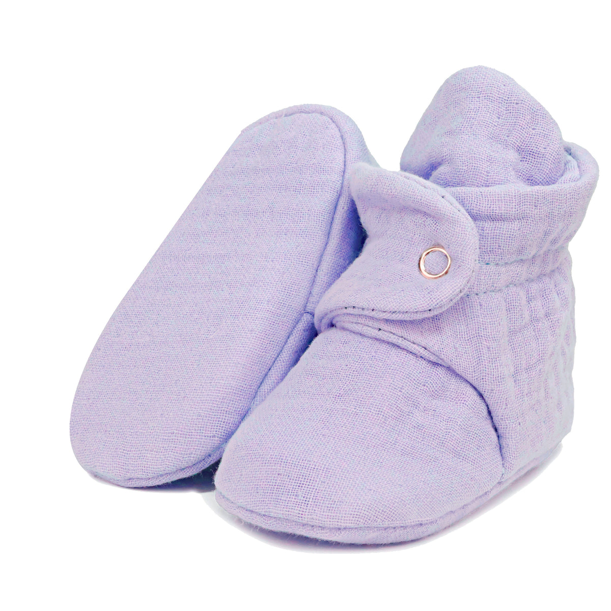 Lilac textured muslin baby booties with snap straps, with one sole facing the camera on a white background.