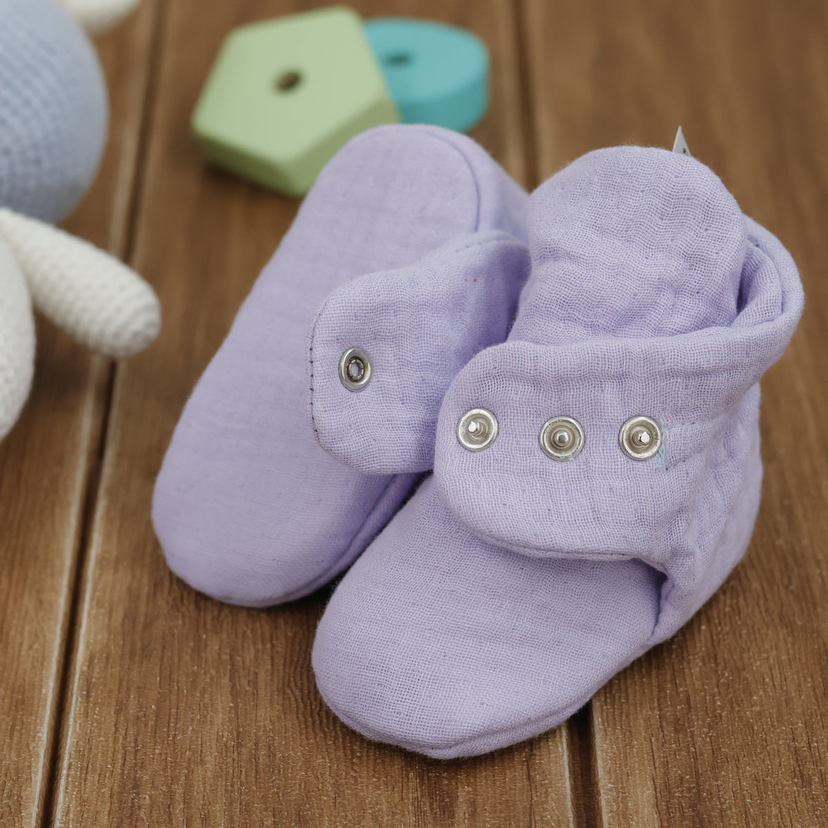 Close-up of lilac textured muslin baby booties with snap straps, showing one sole and an open snap strap.