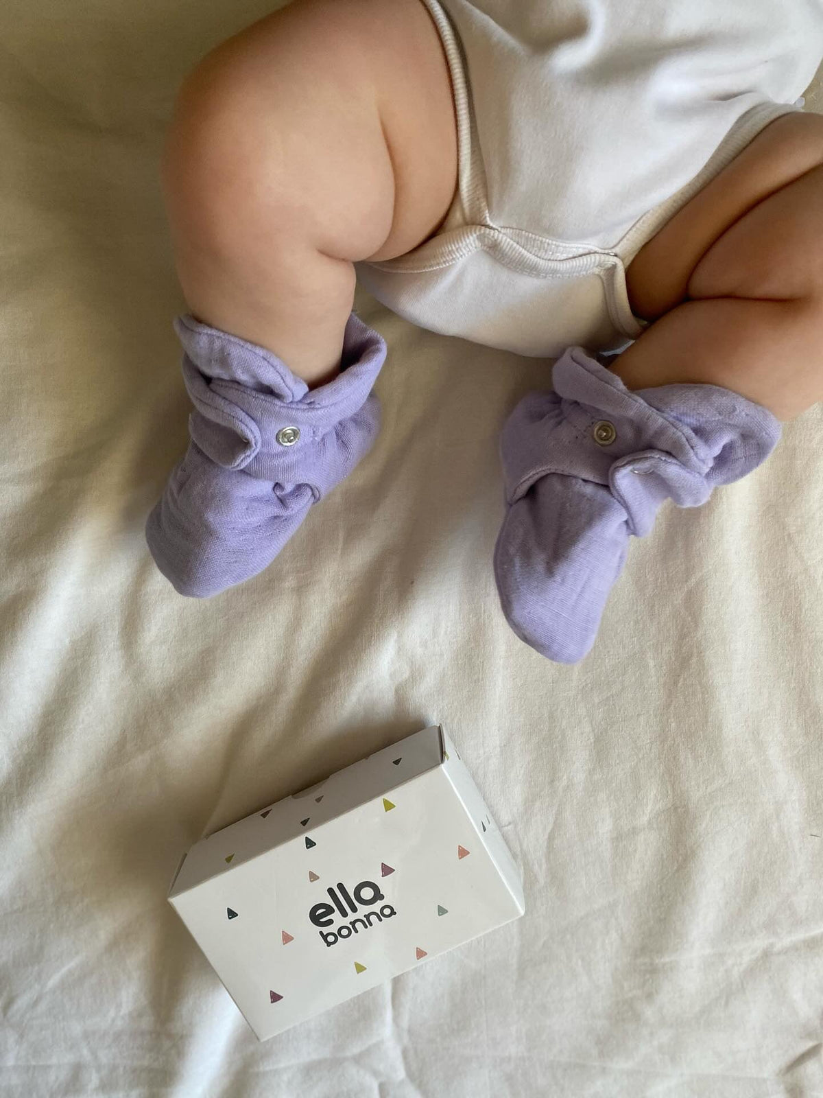 Close-up of lilac booties worn by a baby lying on a blanket.