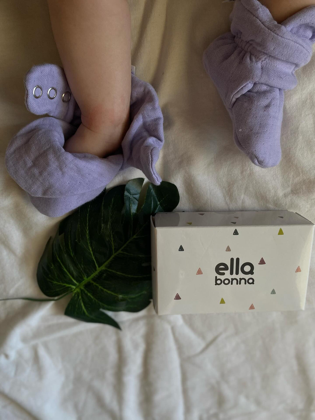 Lilac booties worn beside an Ella Bonna card and a green leaf.