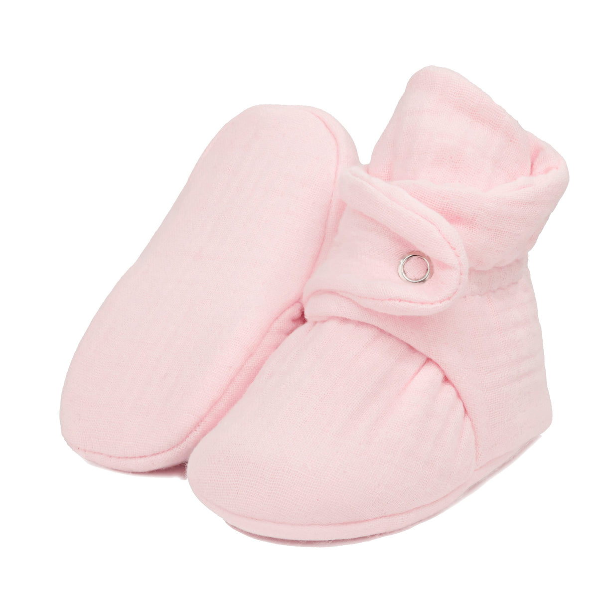 Pale pink textured muslin baby booties with snap straps, with one sole facing the camera on a white background.