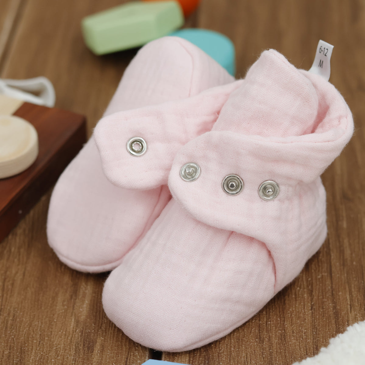 Close-up of pale pink textured muslin baby booties with snap straps, showing one sole and an open snap strap.