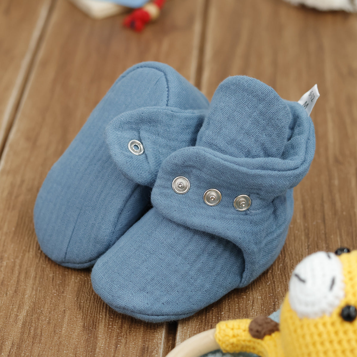 Close-up of muted blue textured muslin baby booties with snap straps, showing one sole and an open snap strap.