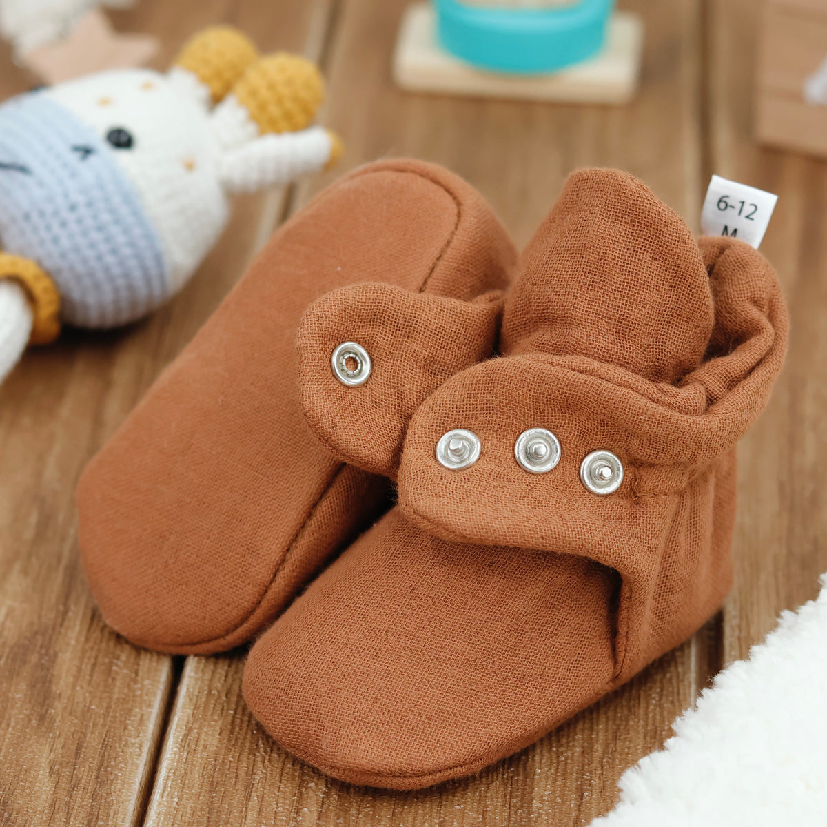 Close-up of warm brown textured muslin baby booties with snap straps, showing one sole and an open snap strap.