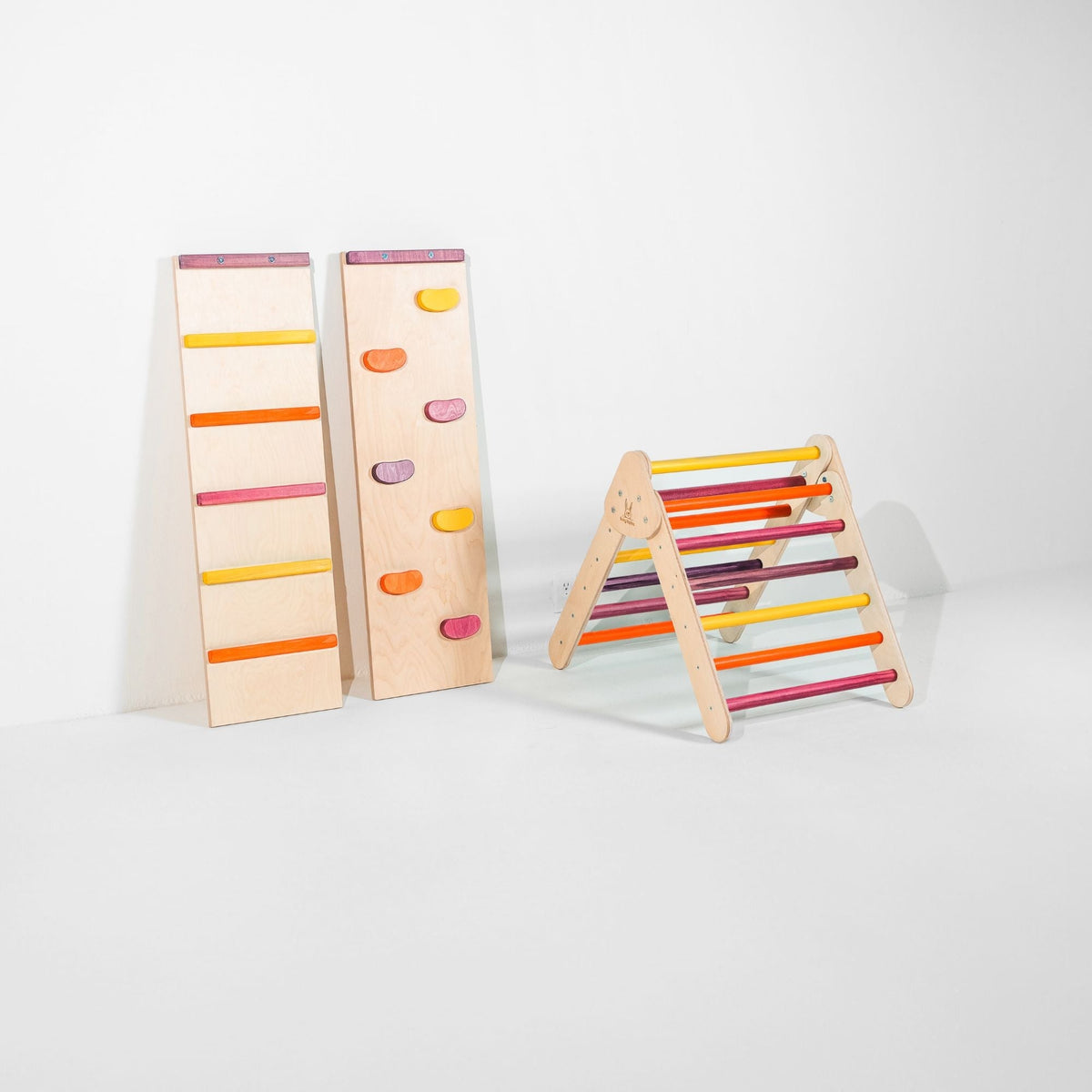 Small pink, purple, orange and yellow climbing triangle beside two upright ramps.