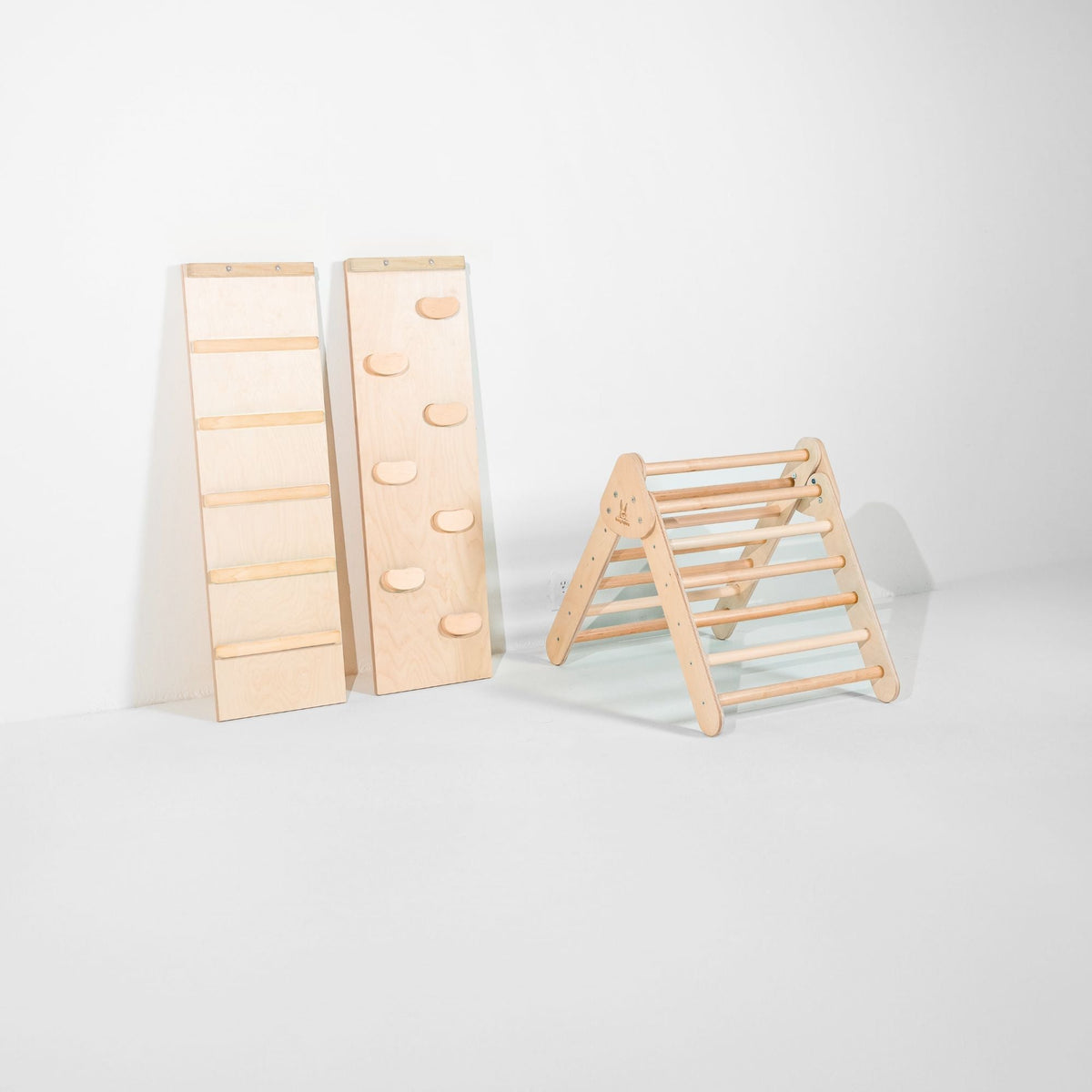 Small light natural-tone climbing triangle beside upright ladder and climbing-hold ramps.