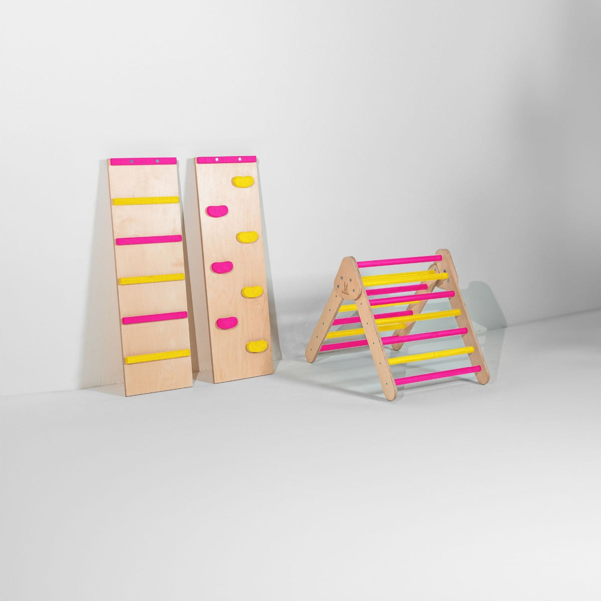 Small bright pink and yellow climbing triangle beside two upright ramps.
