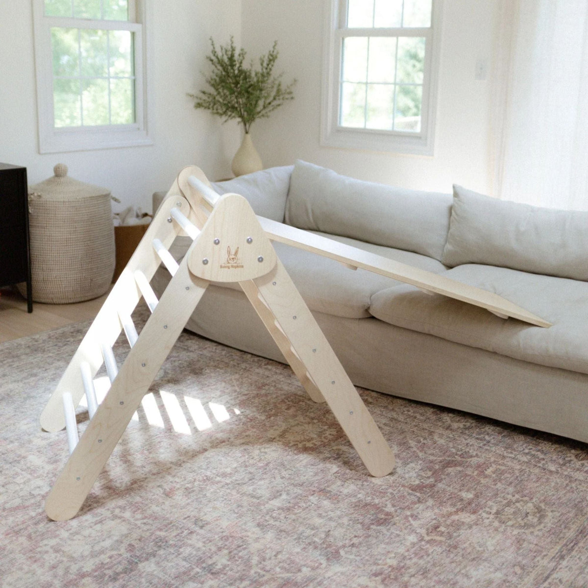 White-rung climbing triangle with a smooth ramp resting on a sofa.