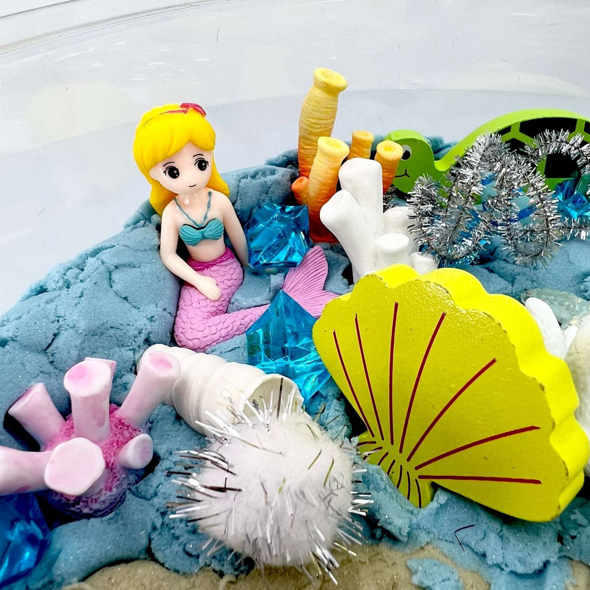 Blonde mermaid figurine beside a shell shape and coral pieces; the blonde mermaid is not included