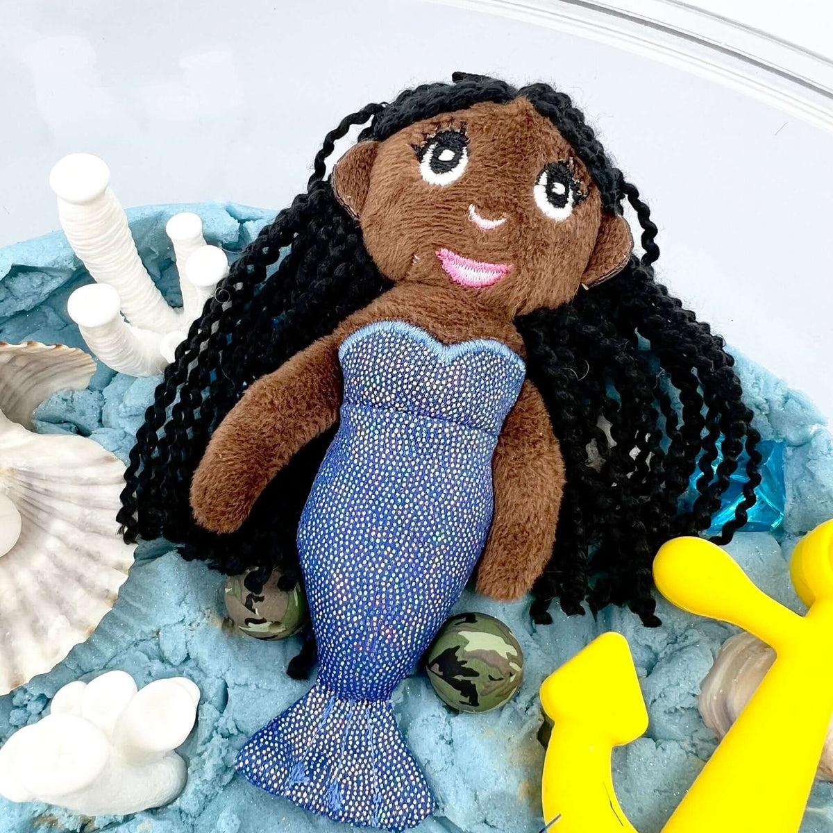 Dark-brown-skinned fabric mermaid doll with black hair and blue tail; the yellow anchor shown is not included