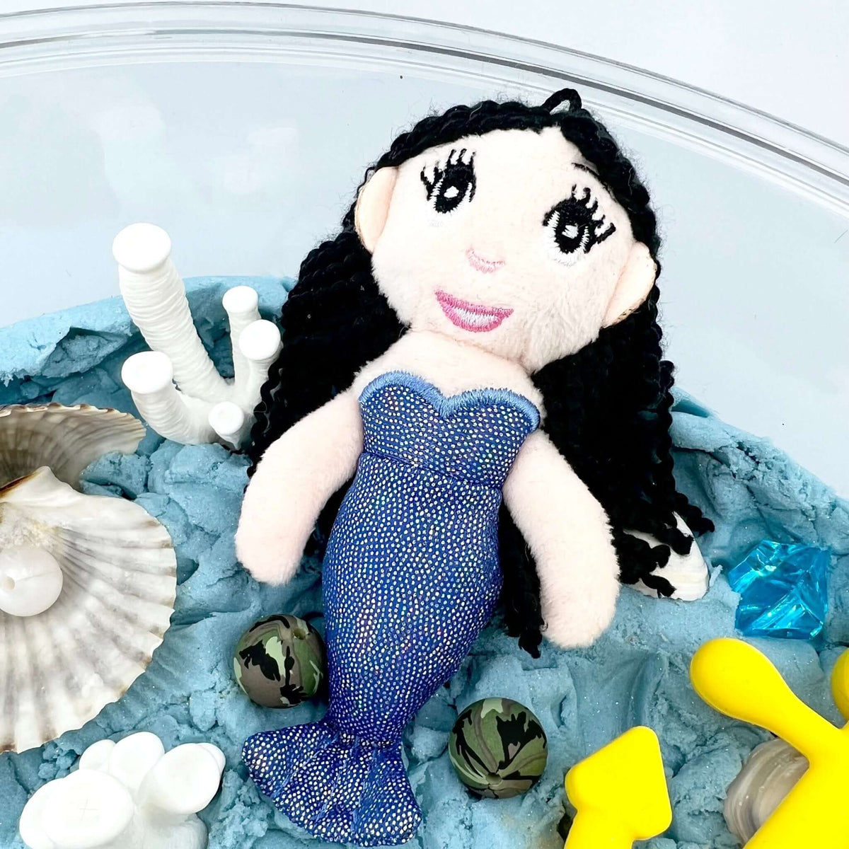 Light-skinned fabric mermaid doll with black hair and blue tail; the yellow anchor shown is not included