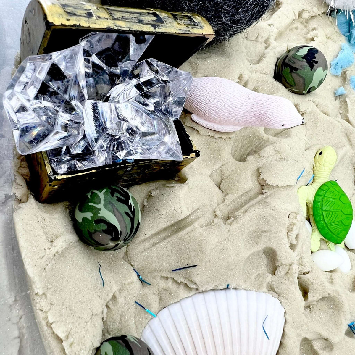 Treasure chest of clear gems beside a seal, turtle and miniature eggs in the sand scene
