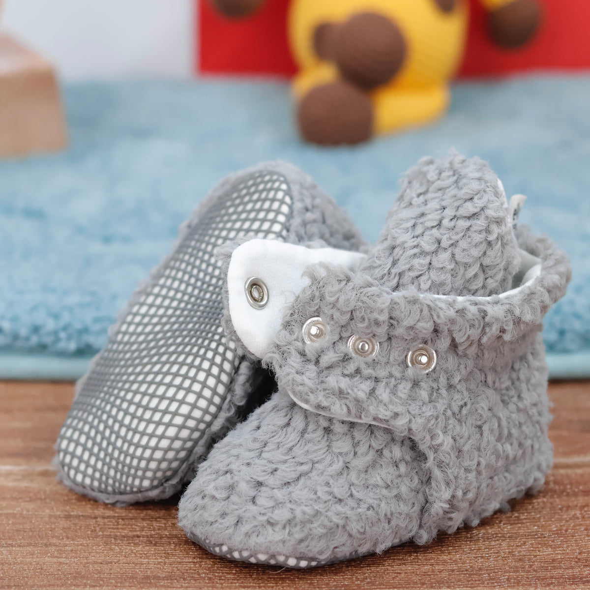 Close-up of gray teddy-texture baby booties with snap straps and gray grip soles, showing one sole and an open snap strap.