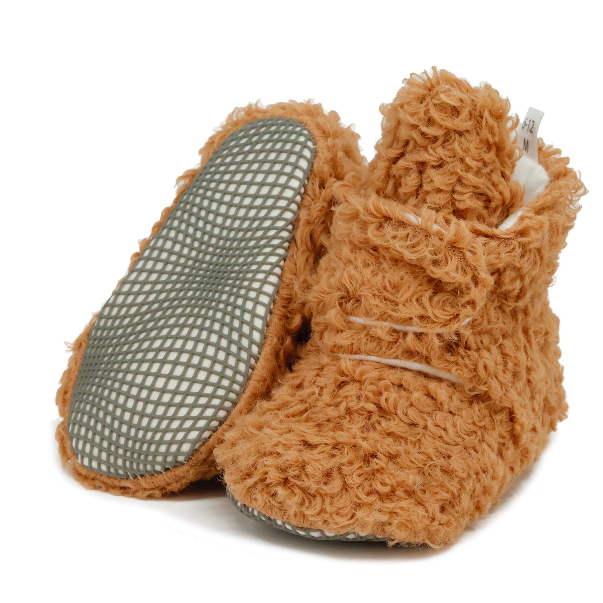 Light brown teddy-texture baby booties with snap straps and gray grip soles, with one sole facing the camera on a white background.