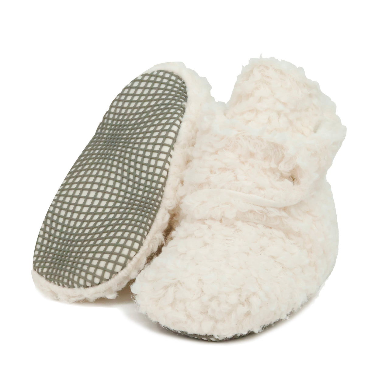 Off-white teddy-texture baby booties with snap straps and gray grip soles, with one sole facing the camera on a white background.