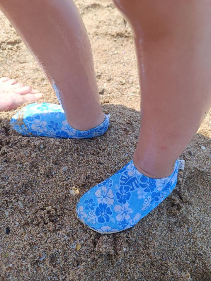 Side close-up of blue floral water shoes worn on sand.