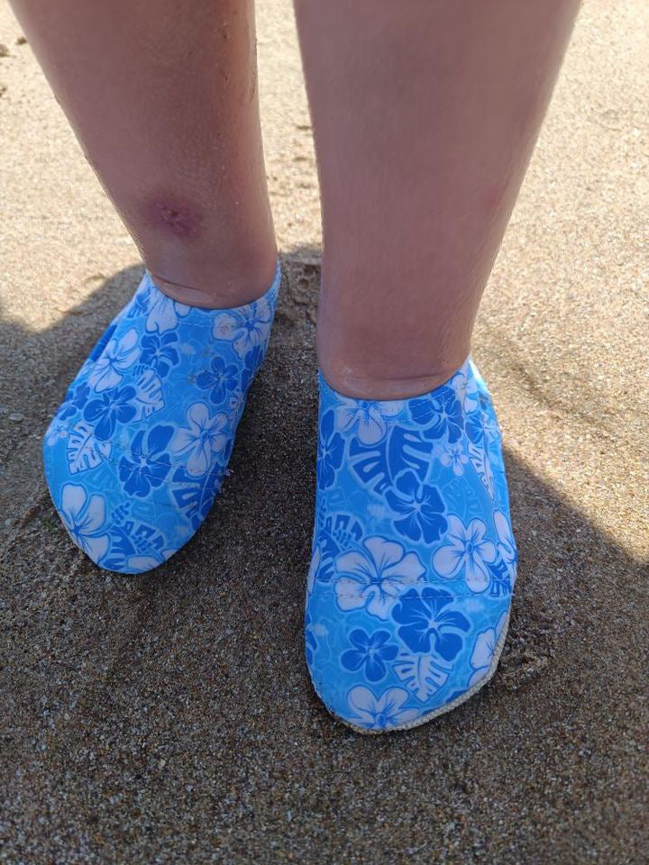 Front close-up of blue floral water shoes worn on sand.