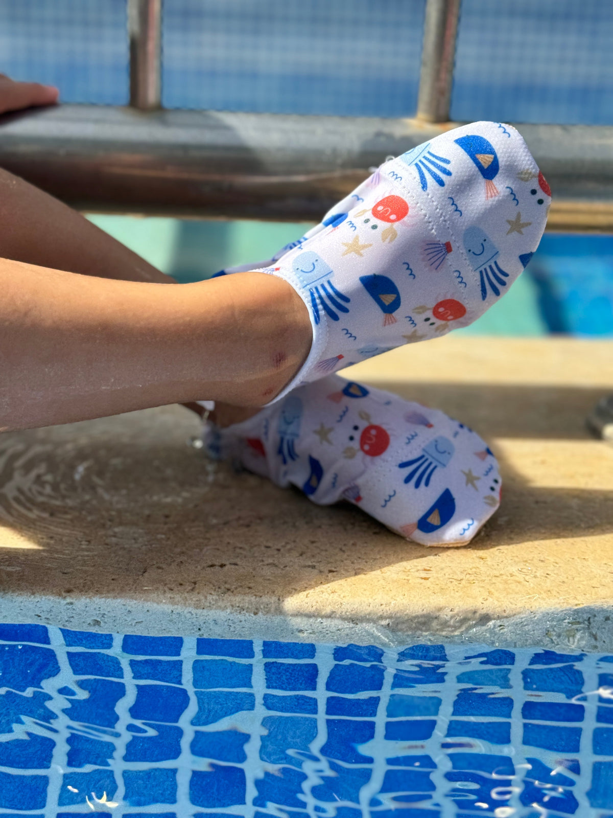 Crab-print water shoes worn while seated at a pool edge.