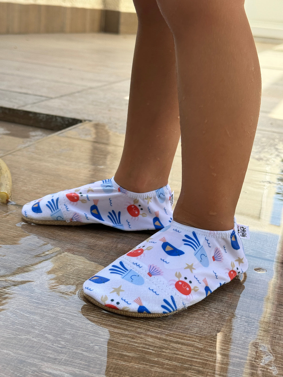 Side view of crab-print water shoes worn on a wet pool deck.