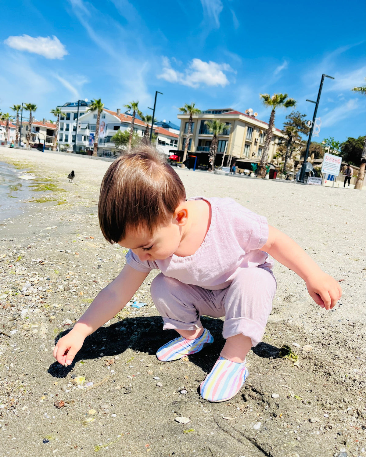 Closer view of a child crouching on sand in striped water shoes.