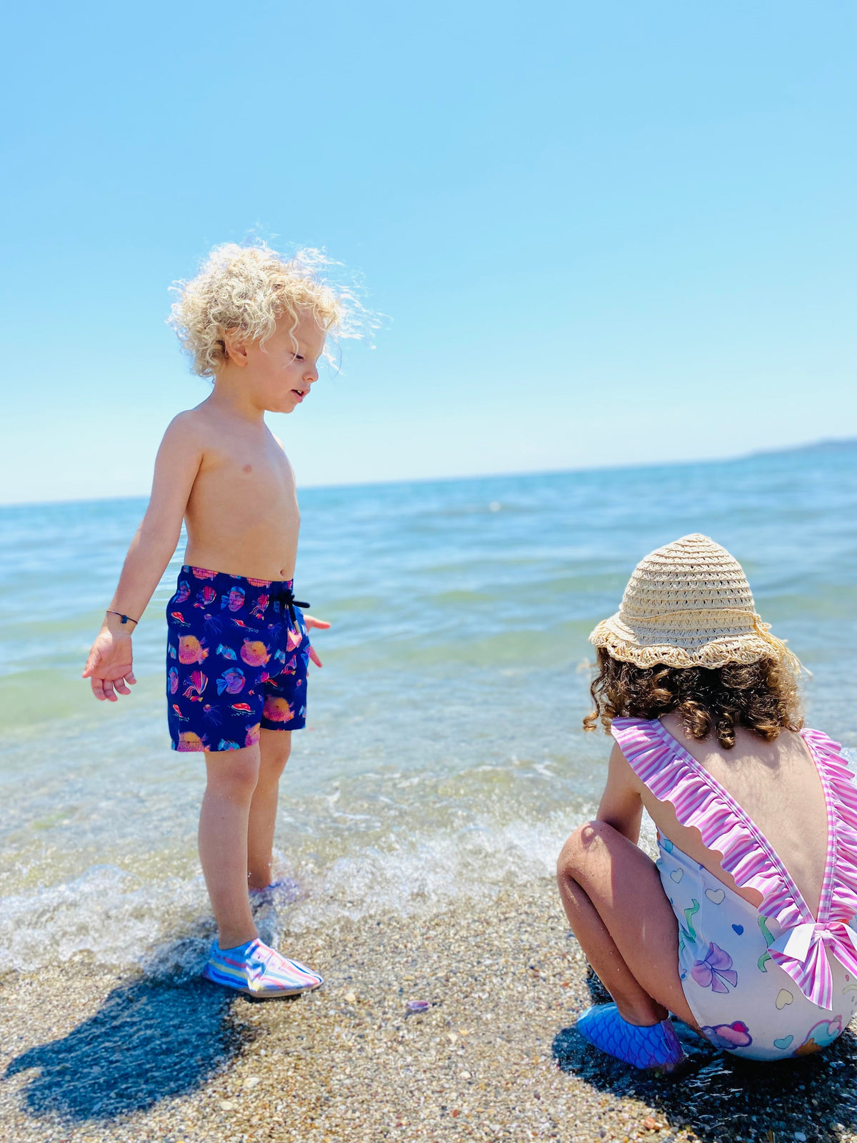 Children at the shoreline wearing water shoes.