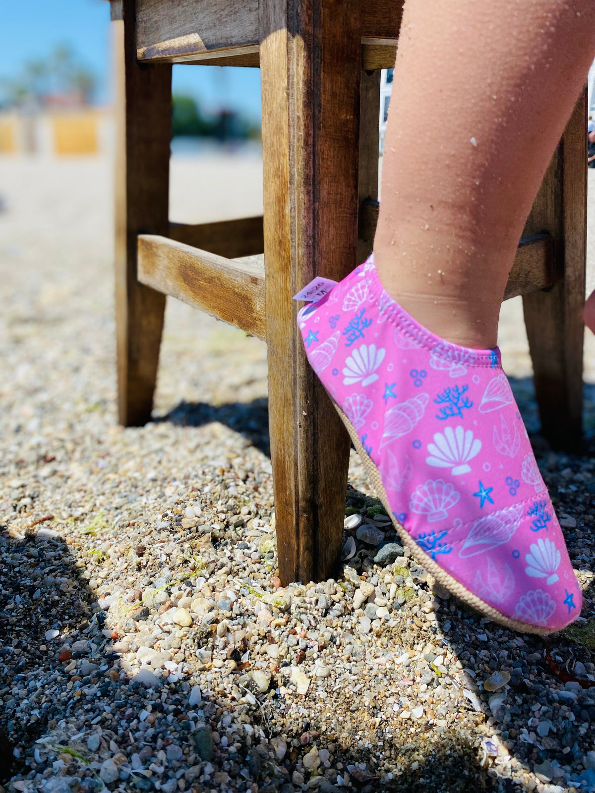 Side close-up of pink shell-print water shoes worn beside a beach chair.