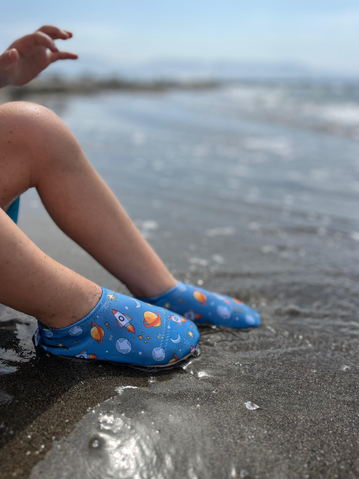 Space-print water shoes worn while seated at the shoreline.