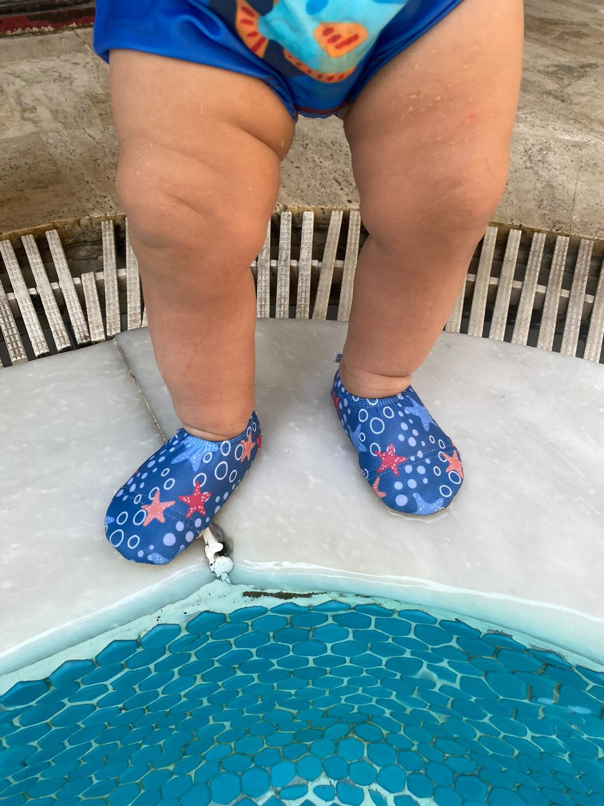 Close-up of starfish-print water shoes worn at a pool edge.