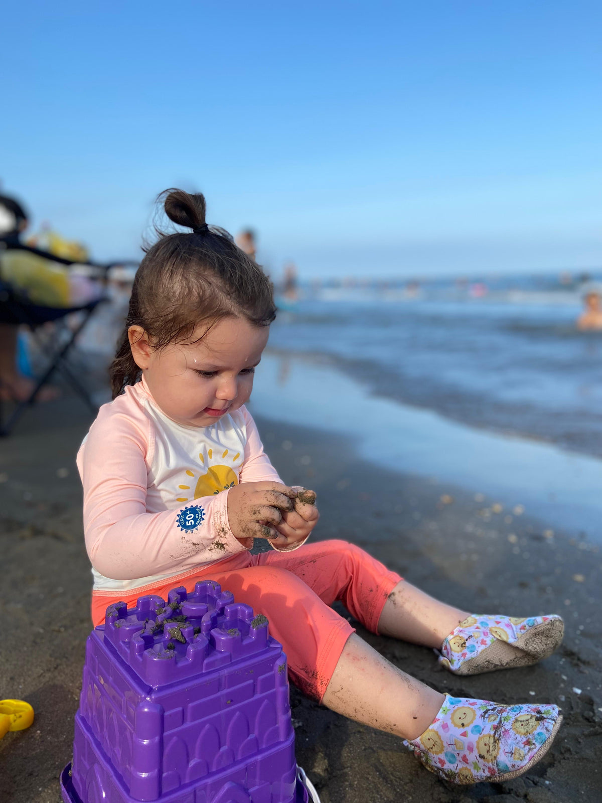 Child seated at the shoreline wearing sun-print water shoes.