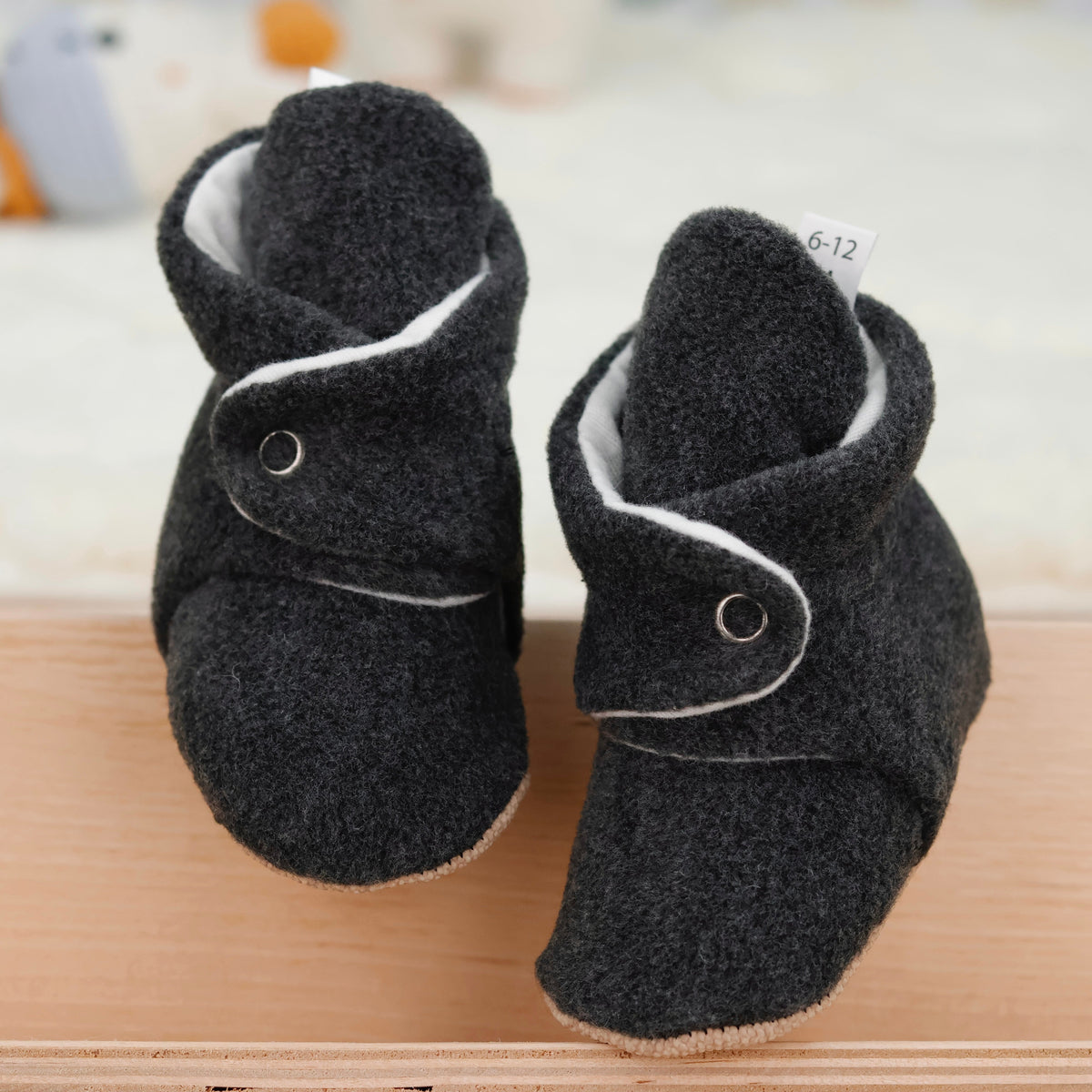 Front view of a pair of charcoal fleece-texture baby booties with snap straps and tan soles.