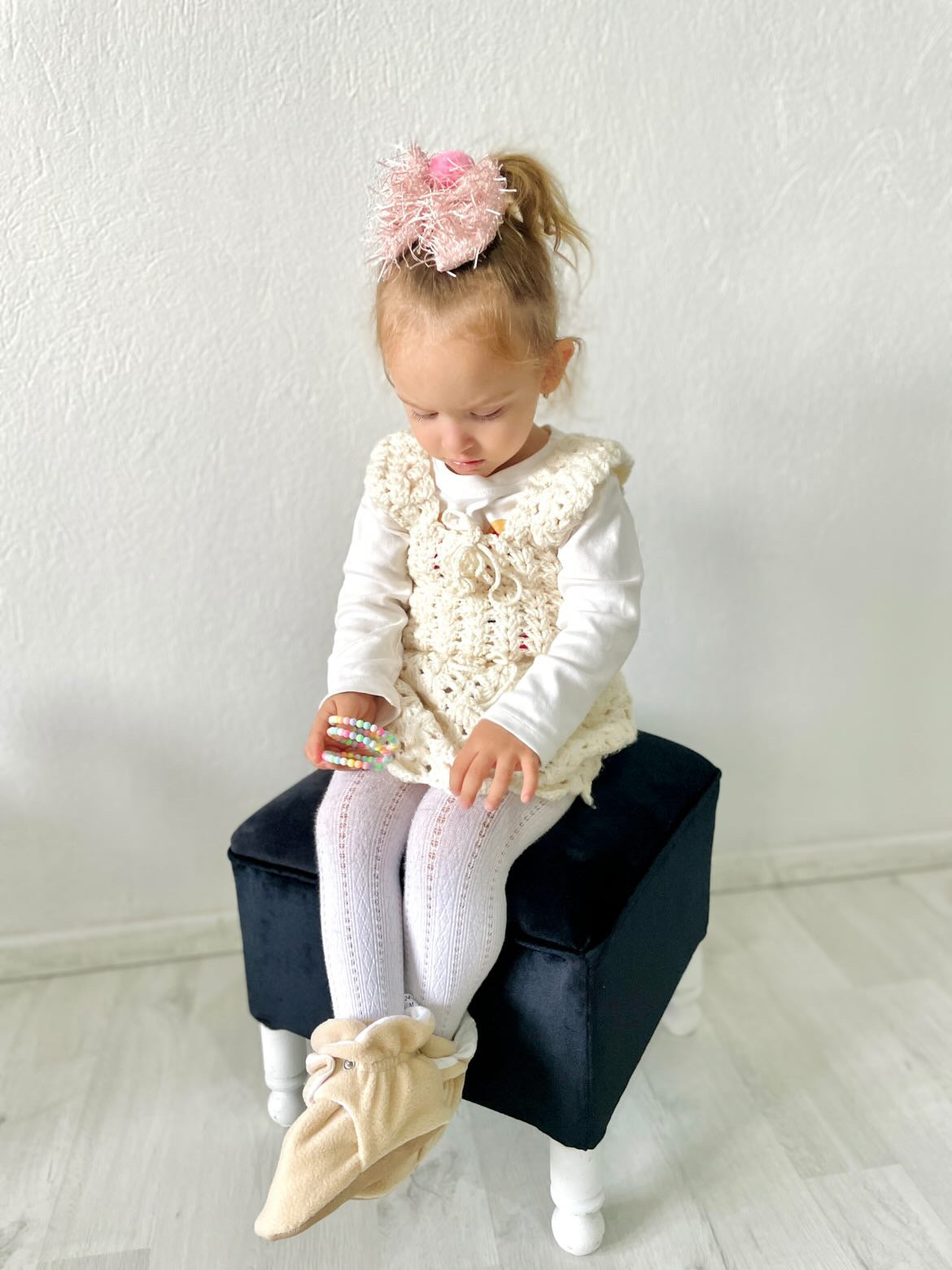 Child seated on a small chair wearing beige booties.