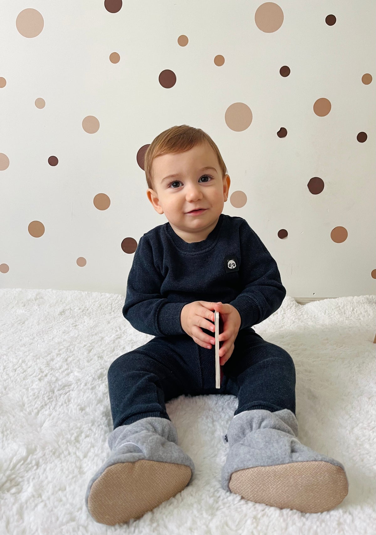 Child seated on a couch wearing gray booties with tan soles visible.