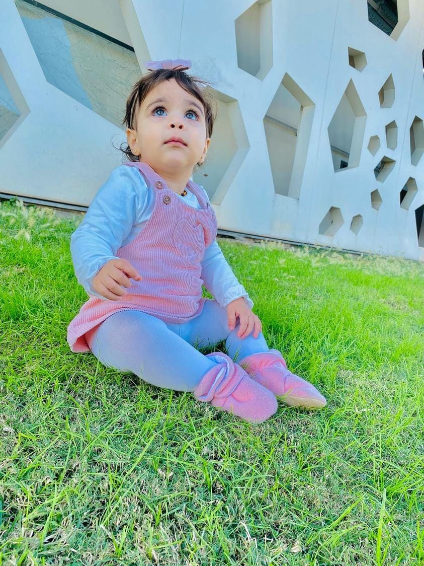 Child seated on grass wearing pink booties.