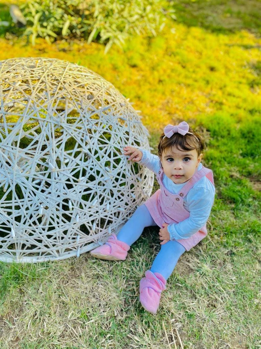 Child seated on grass beside a decorative chair wearing pink booties.