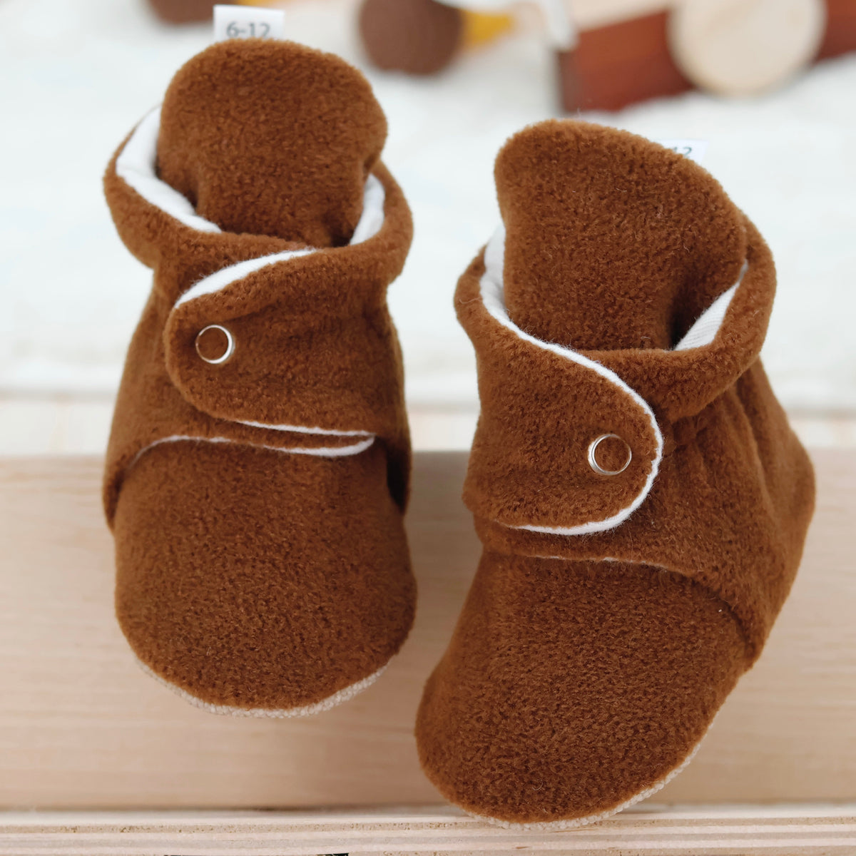 Front view of a pair of warm brown fleece-texture baby booties with snap straps and tan soles.