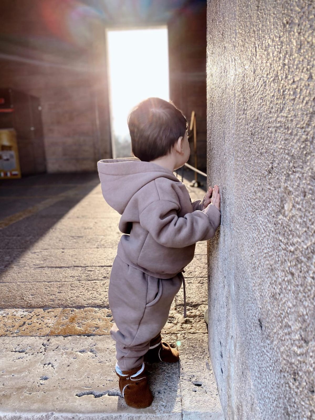Child standing beside a stone pillar wearing brown booties.