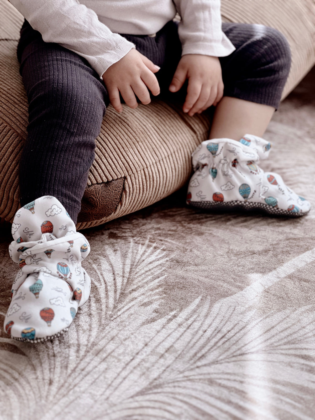 Child seated on a cushion wearing balloon-print booties.