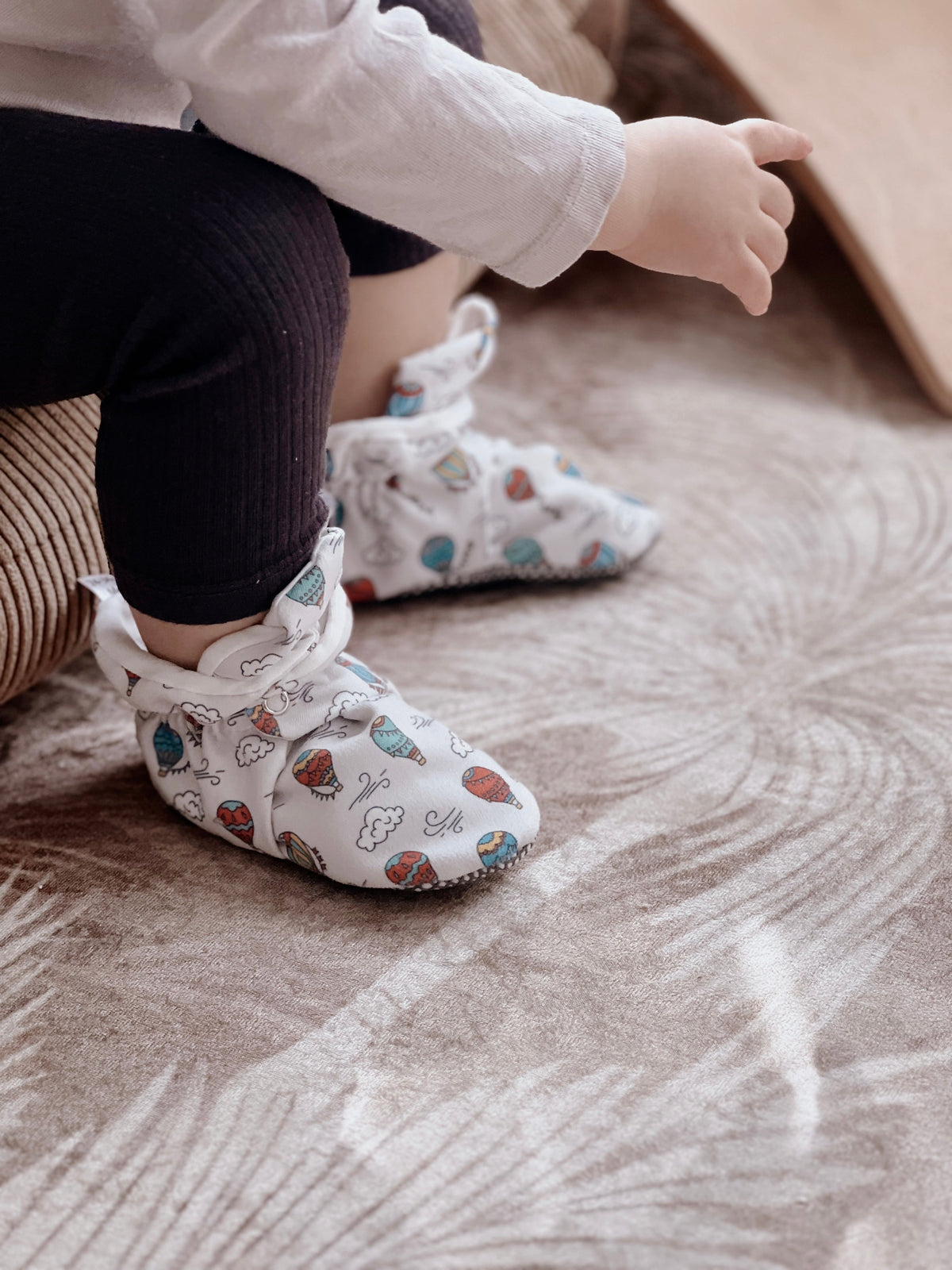Side view of balloon-print booties worn by a seated child.