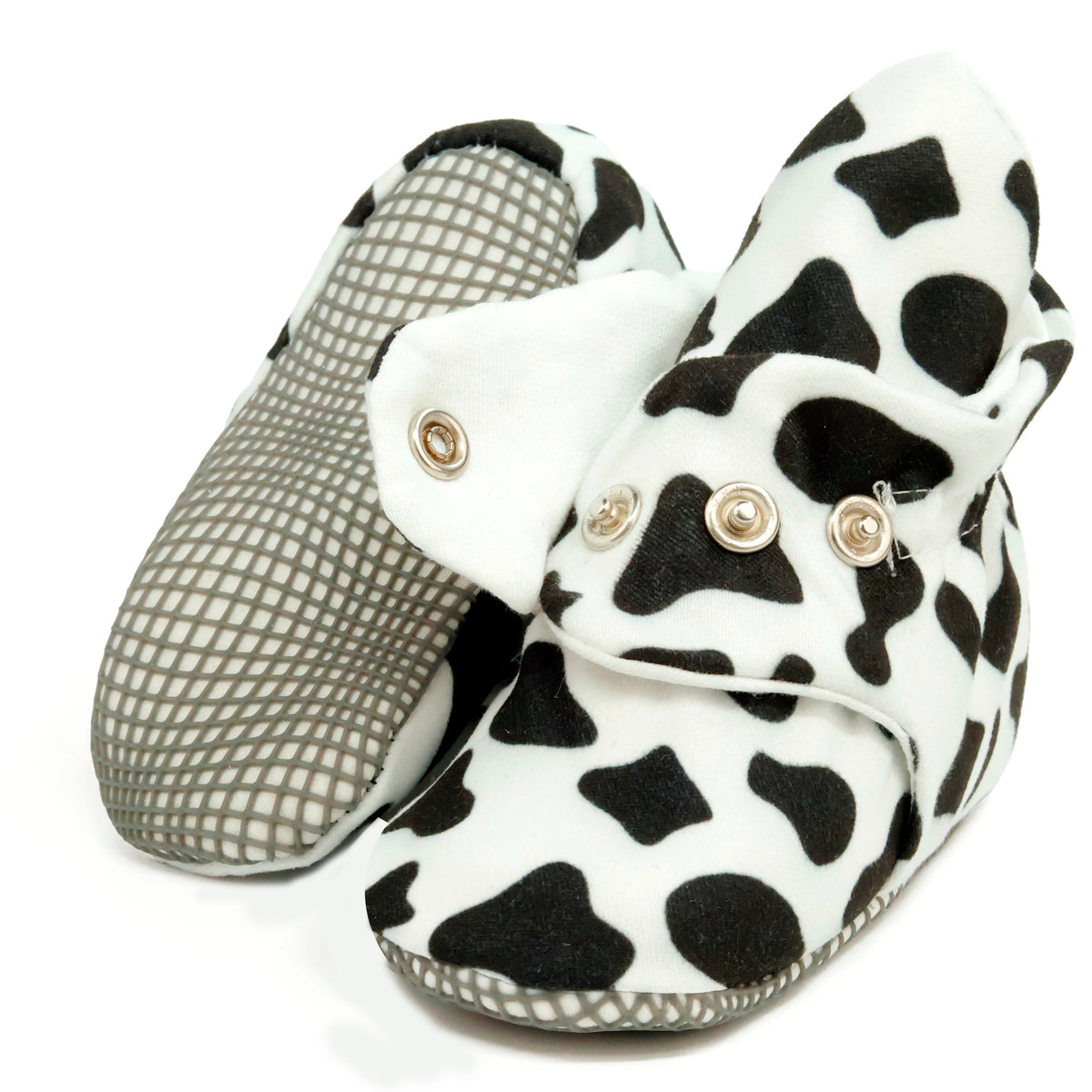 White baby booties with black cow spots and snap straps, showing one sole and an open snap strap on white.