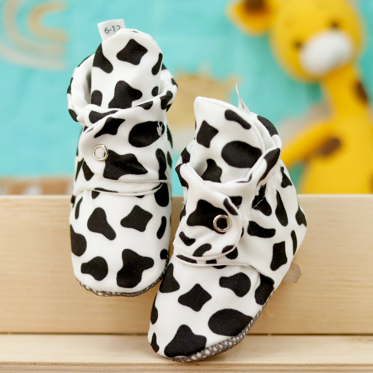 Front view of a pair of white baby booties with black cow spots and snap straps.