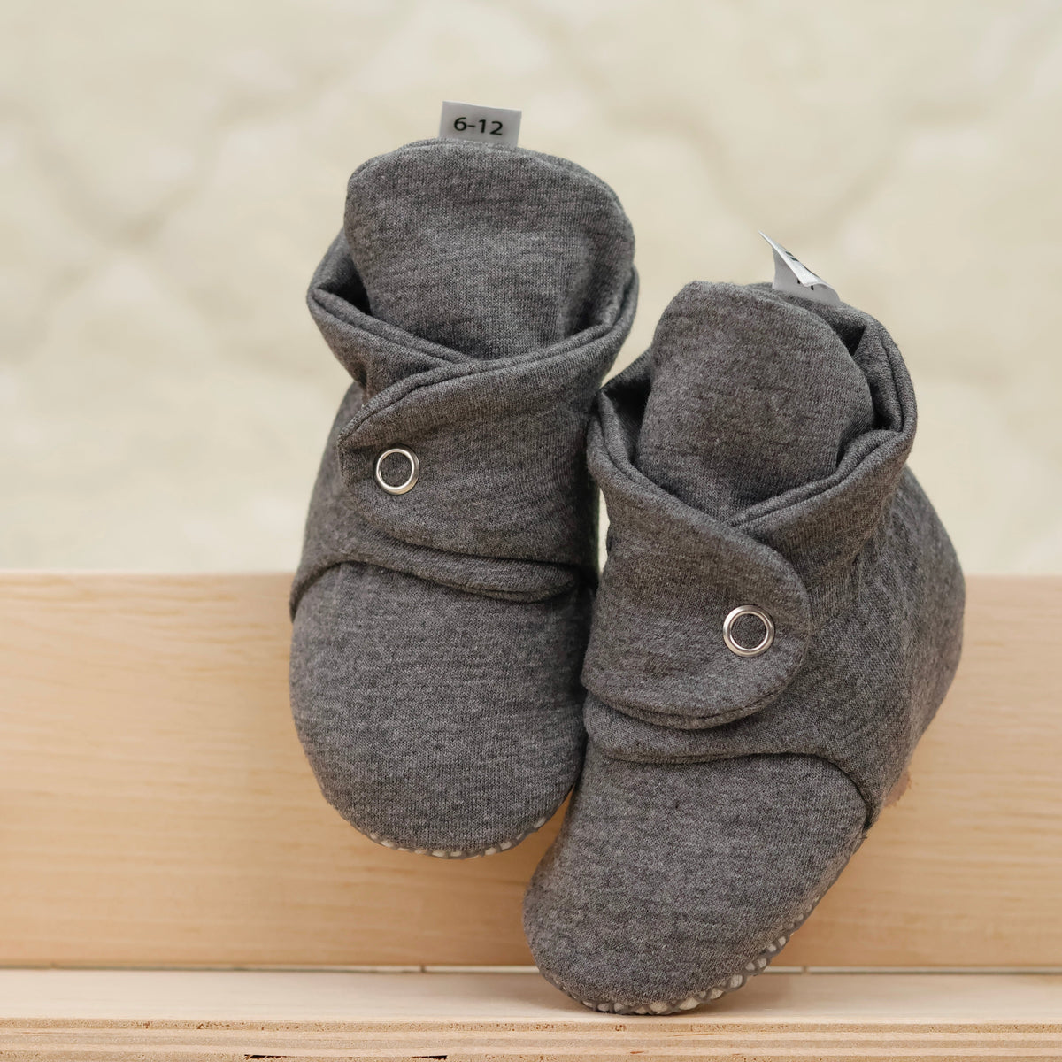 Front view of a pair of dark gray fabric baby booties with snap straps and gray grip soles.